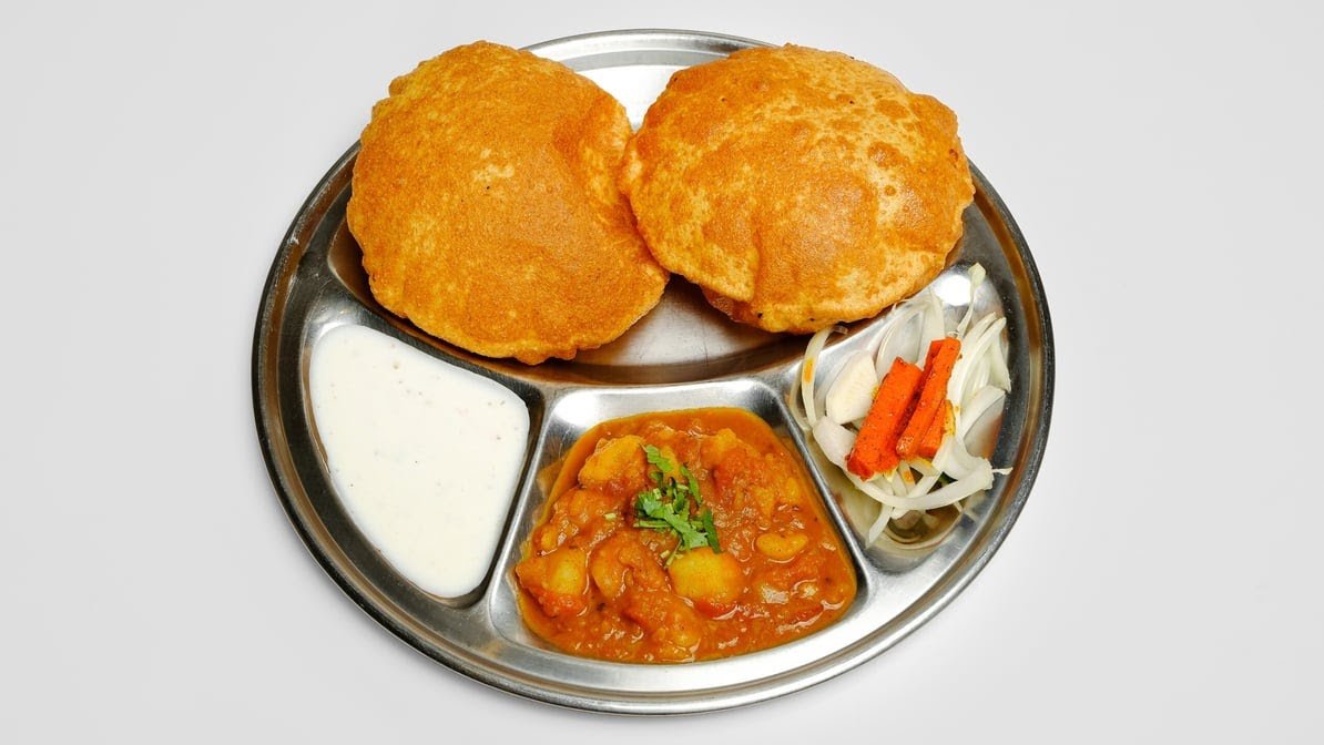 Aloo puri plate with golden puris, potato curry and raita